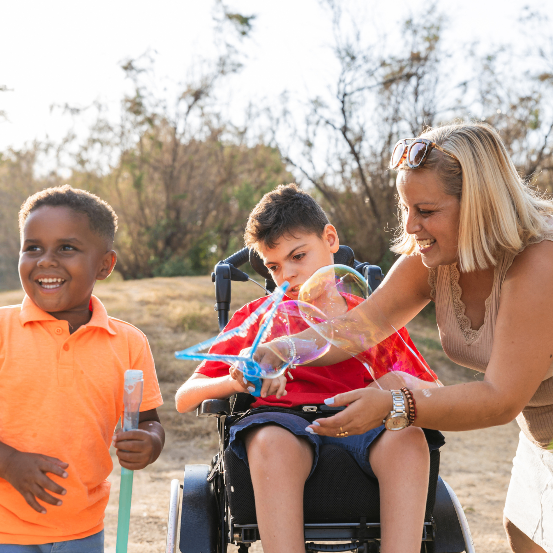 Educator supporting a child in a wheelchair blowing bubbles with a friend